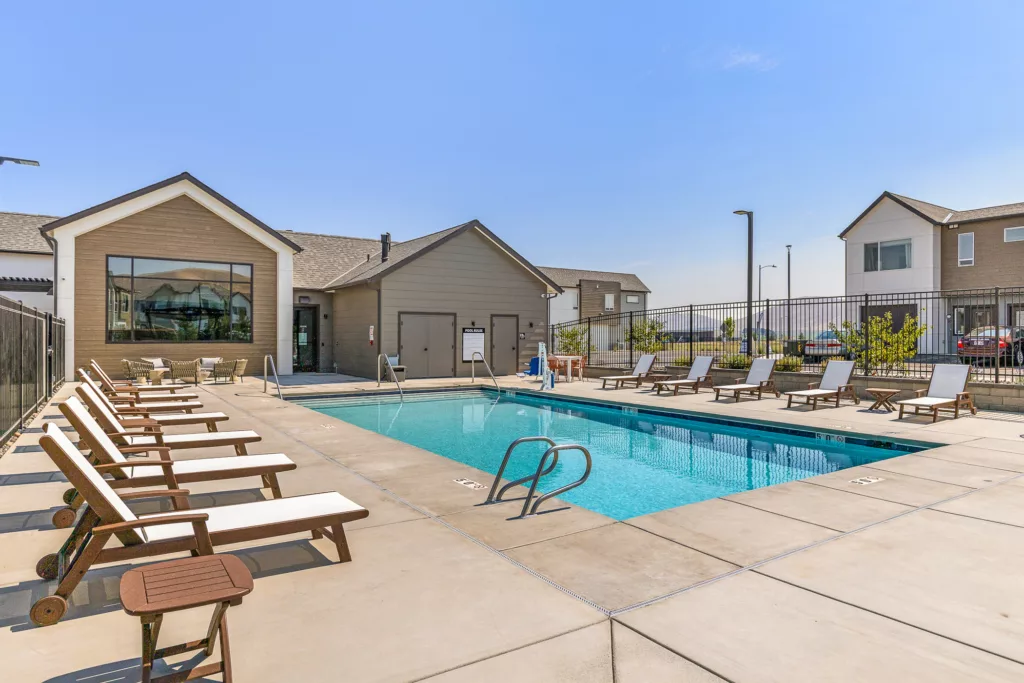 Outdoor swimming pool with a row of lounge chairs and a modern building in the background, under a clear blue sky.