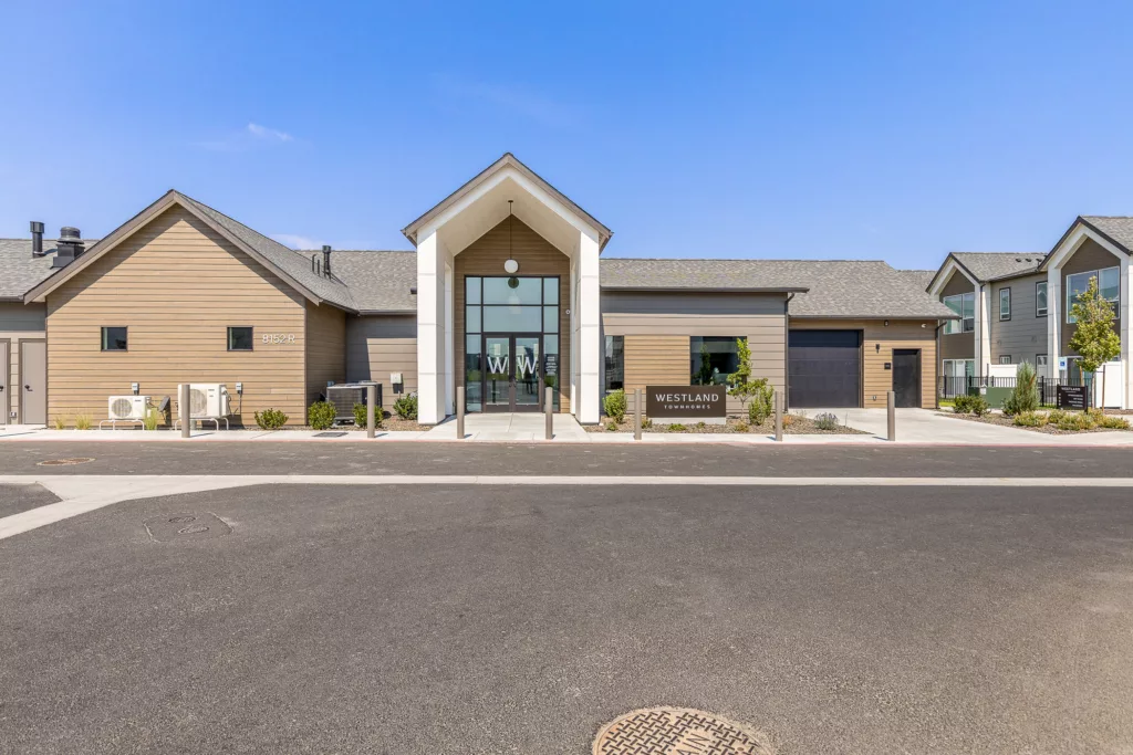 A modern building labeled "Westland Townhomes" with a glass entrance, beige siding, and a pitched roof, surrounded by a neatly landscaped area.