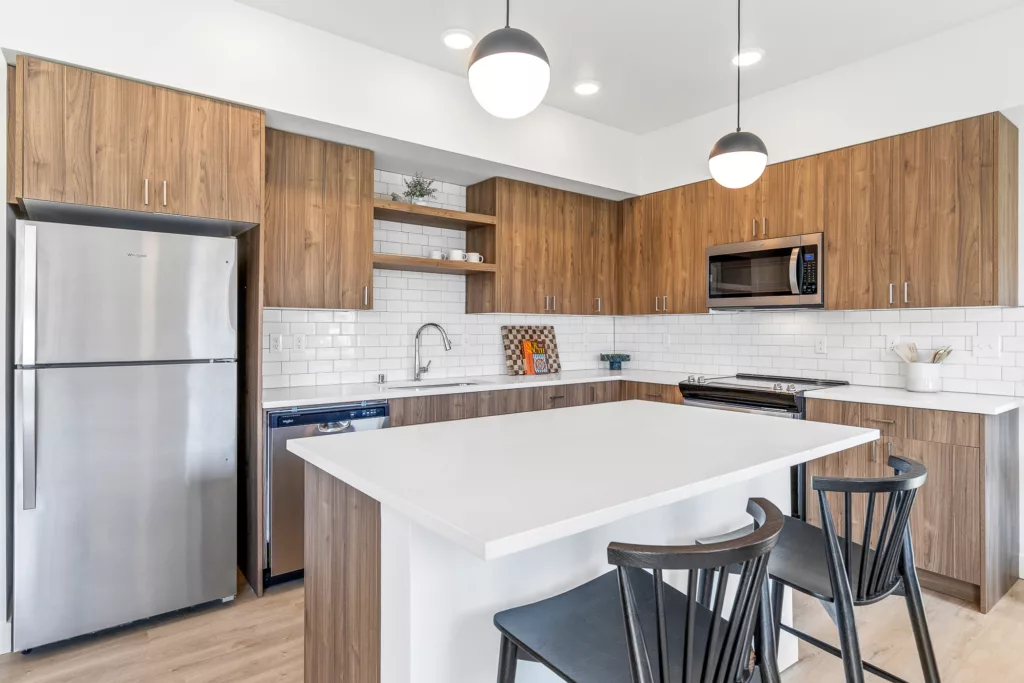 Modern kitchen with wooden cabinets, a large white island, stainless steel appliances, and two pendant lights.