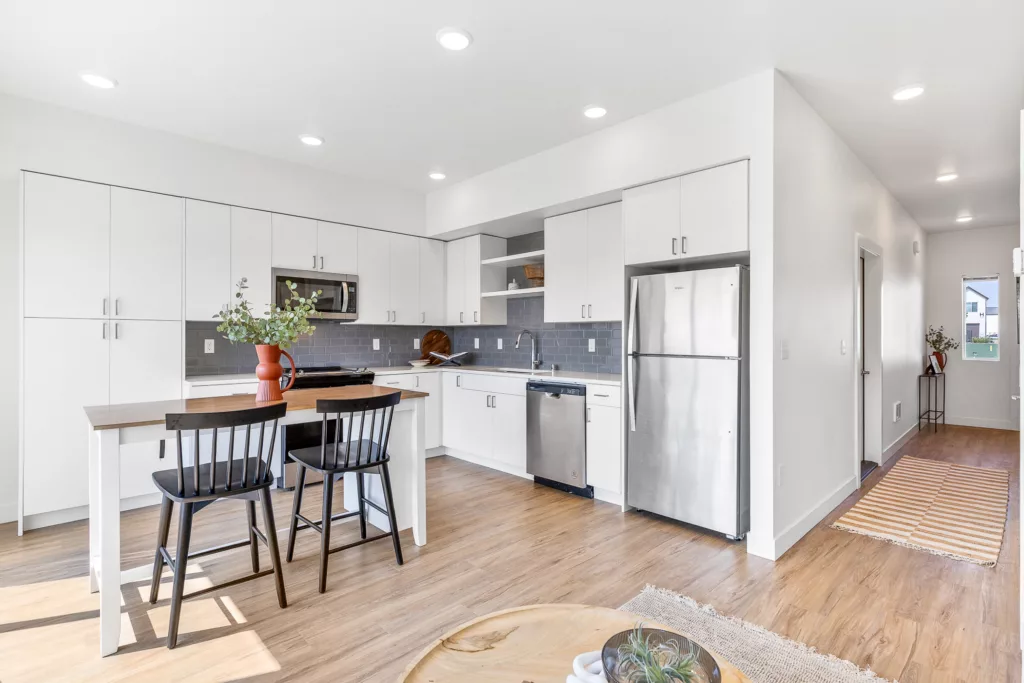 Modern kitchen with white cabinets, stainless steel appliances, a wooden island with black chairs, and a vase with greenery on the counter.