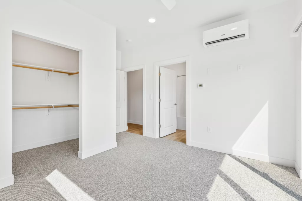 Bright empty room with carpeted flooring, a built-in closet, white walls, and a ceiling-mounted air conditioning unit.